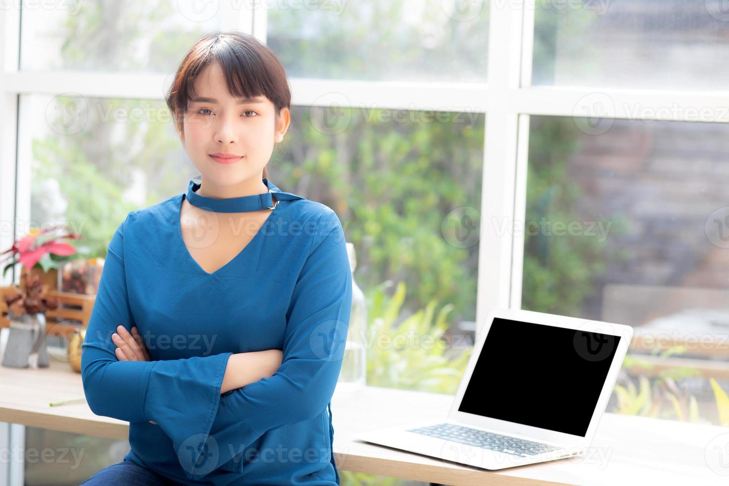 Beautiful of portrait asian young woman sitting looking camera and laptop on table at coffee shop, professional female freelance using notebook computer with connect to internet job. photo