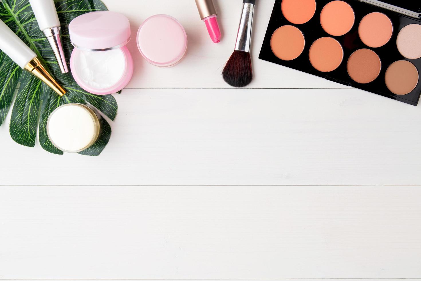 cosmetic and skin care product and green leaves on white wood table, beauty with treatment cream and moisturizer on wooden desk, health and wellness concept, top view. photo