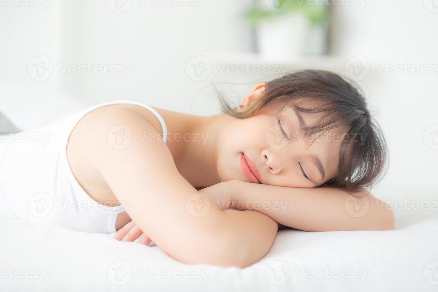 hermosa mujer joven asiática sonríe durmiendo acostada en la cama con un ocio cómodo y feliz en el dormitorio, bienestar de la niña asiática de belleza con relajación y fresco para el concepto de salud. foto