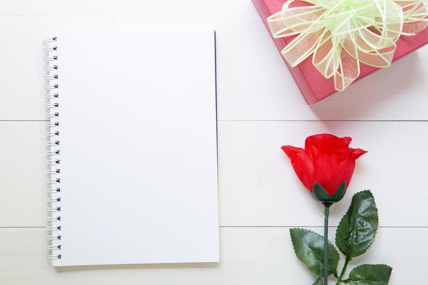 Present gift with red rose flower and notebook with copy space on wooden table, 14 February of love day with romantic, valentine holiday concept. photo