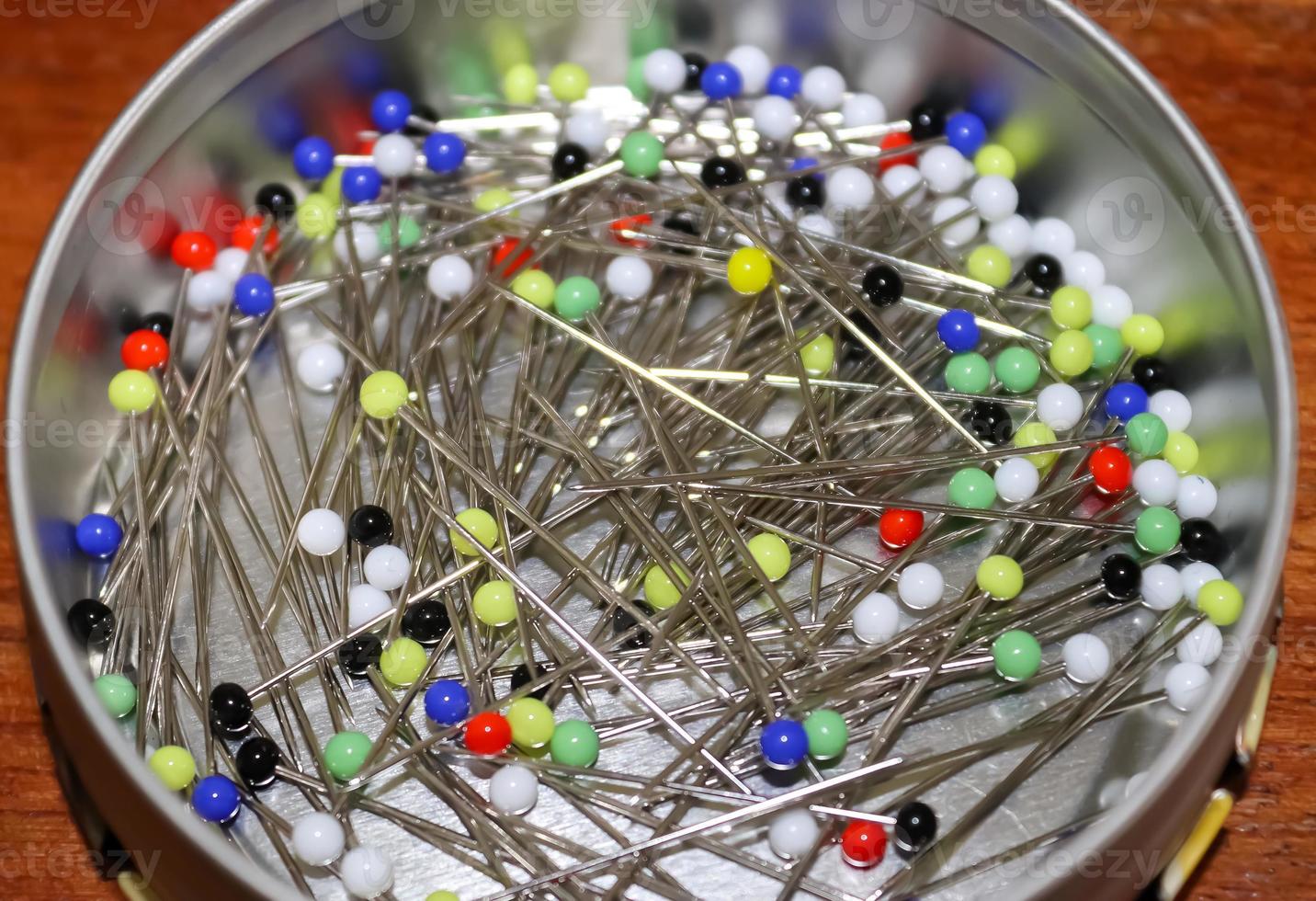 Close up view on lots of sewing pins with colored heads in a metal box on a wooden table photo