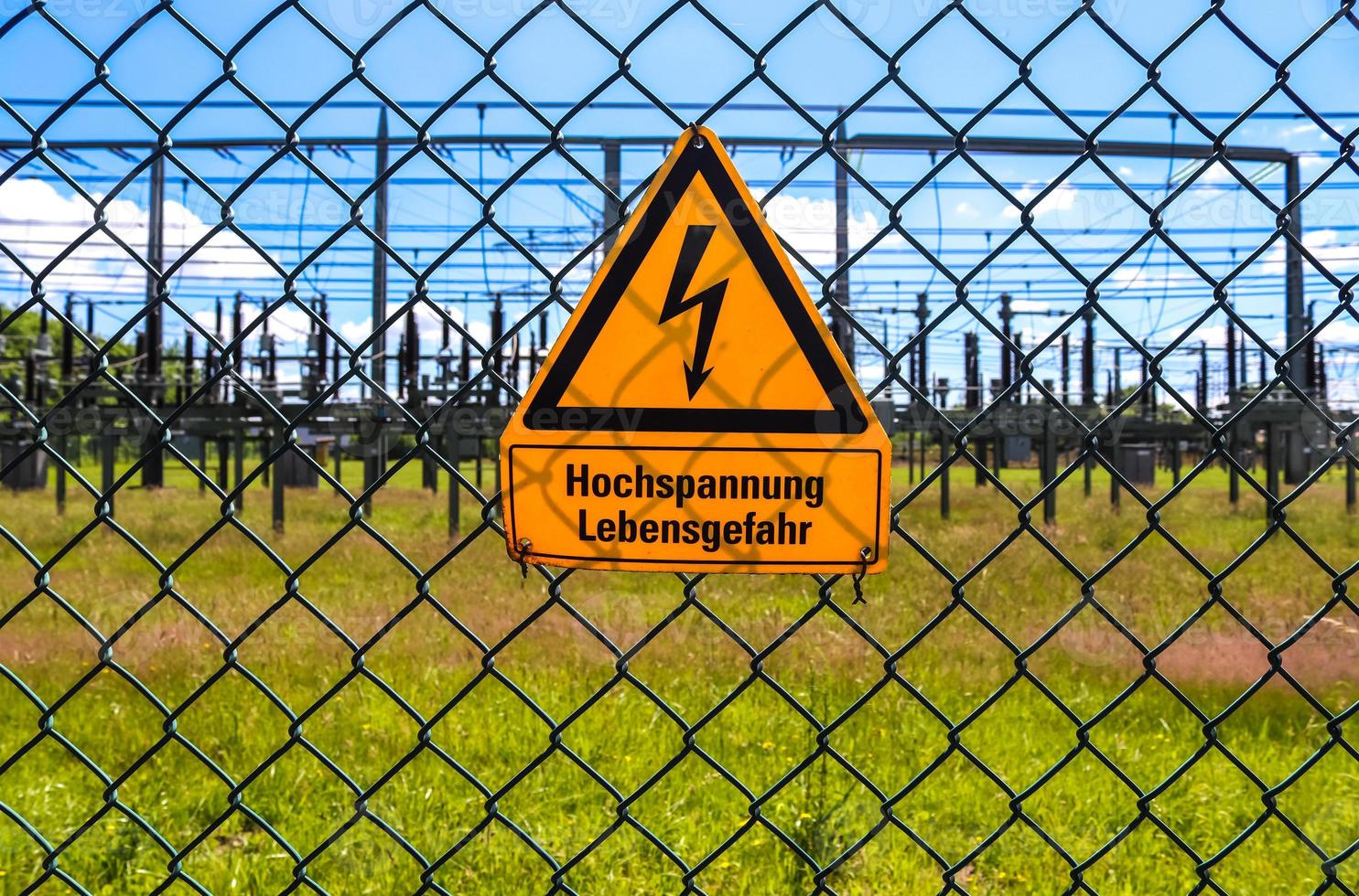 Sign showing the words high voltage in german language at the fence of a big substation distributing electric energy with lots power lines on a sunny day photo