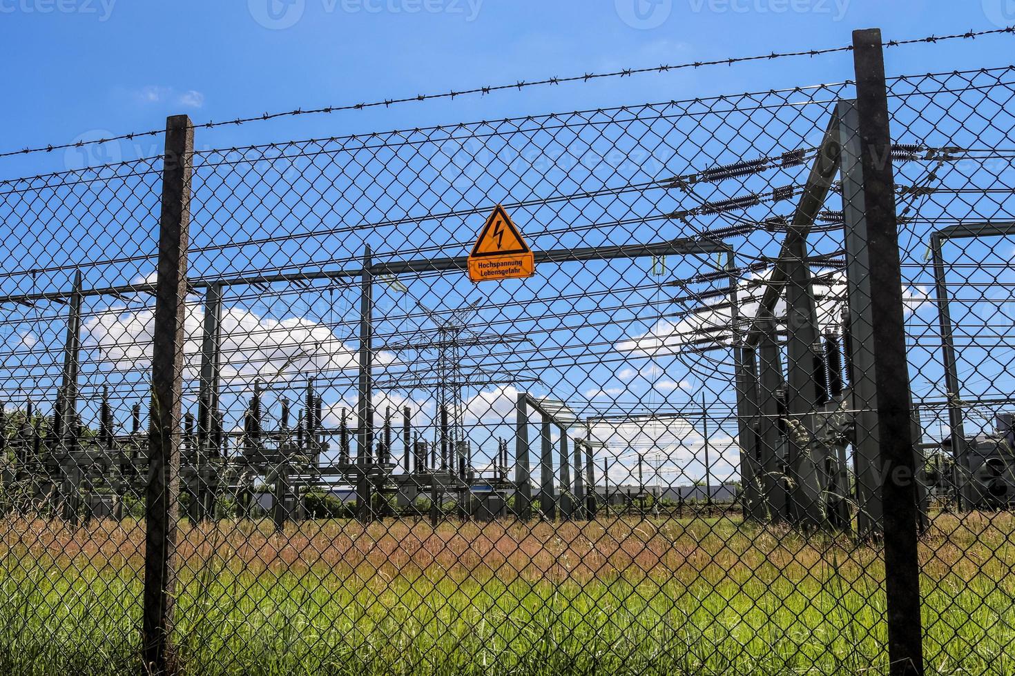 cartel que muestra las palabras alto voltaje en alemán en la cerca de una gran subestación que distribuye energía eléctrica con muchas líneas eléctricas en un día soleado foto