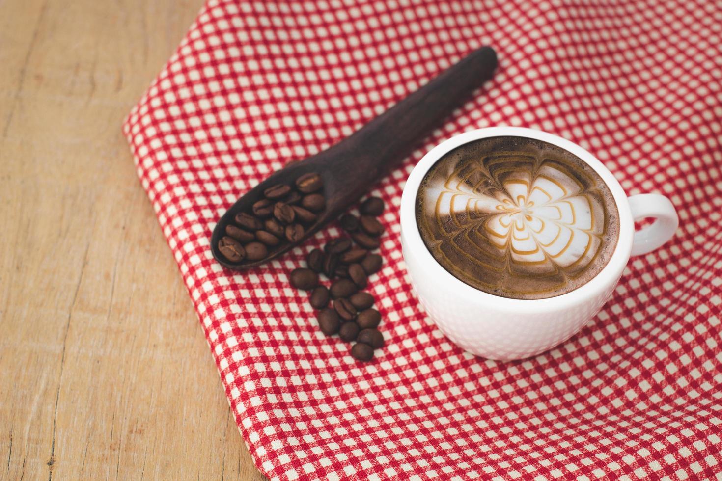 latte coffee in white cup and  beans with red patterned fabric on a wooden background.copy space. photo