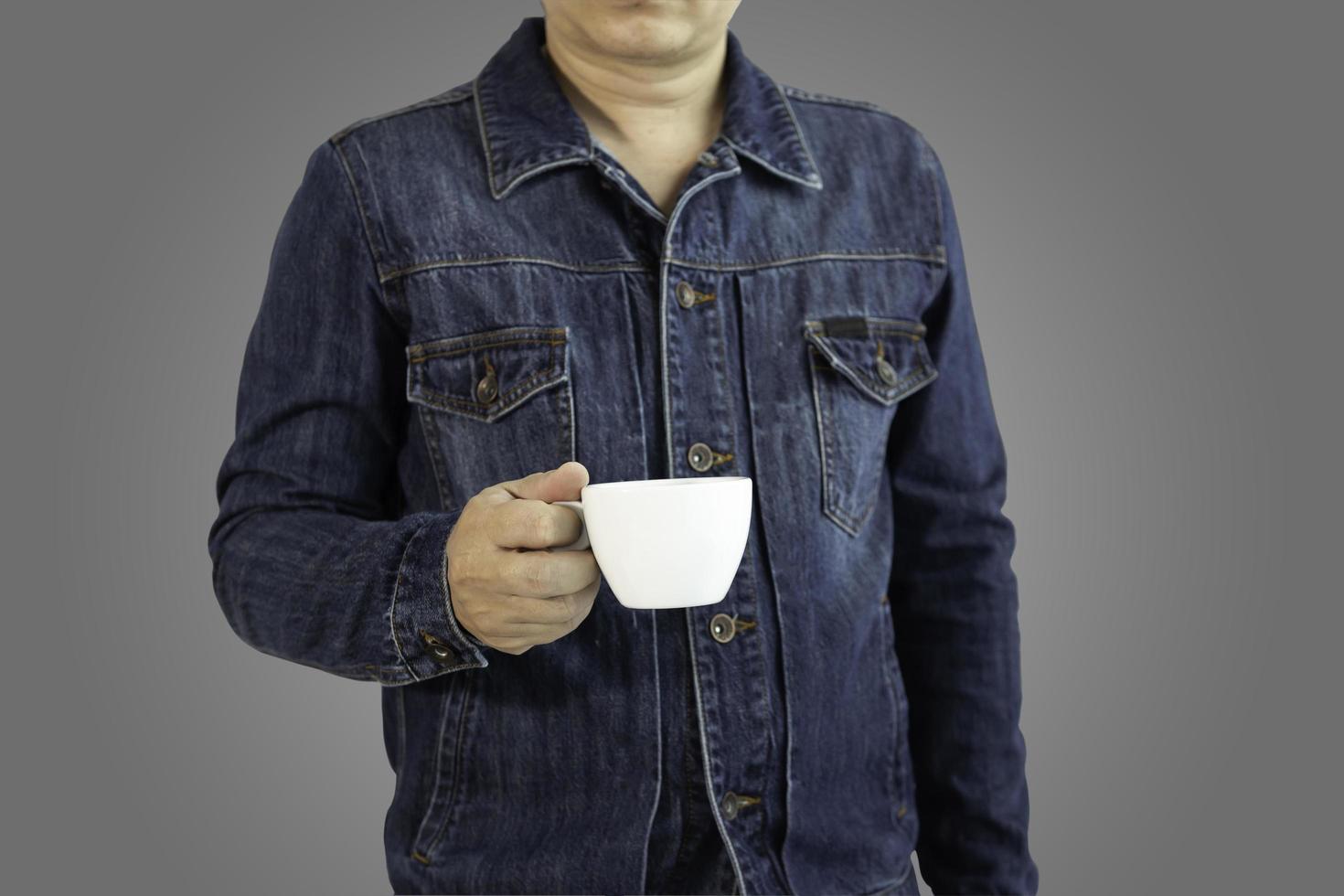 A man in a denim shirt holding a white coffee or tea mug against a gray gradient background with clipping path.selective focus. photo