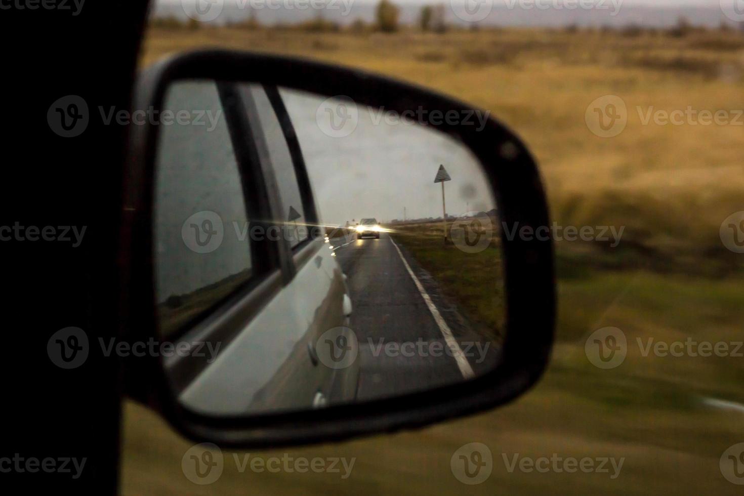 The reflection of road in the side view mirror with raindrops. Travel concept. photo