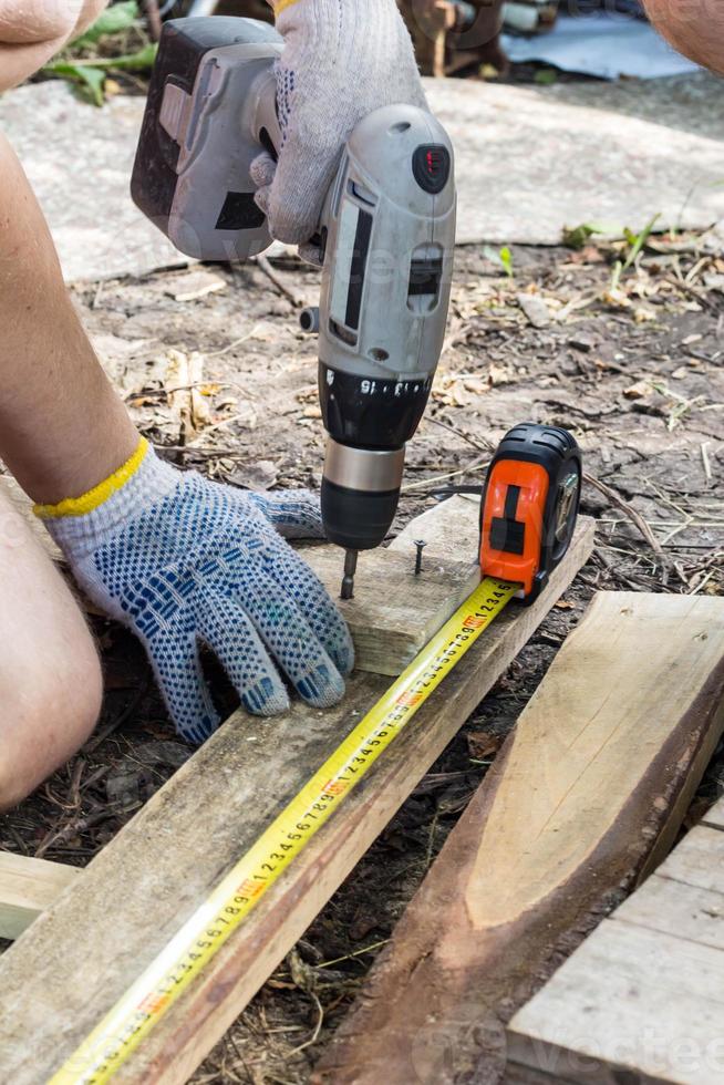 Close up of hands of a carpenter worker screws a bolt in a wooden board with a screwdriver on construction site photo