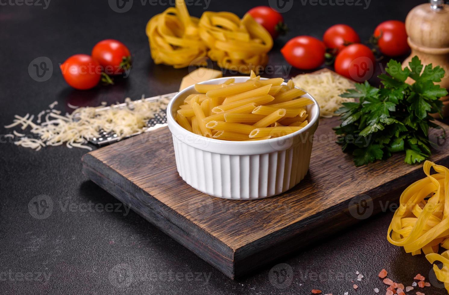 Raw tagliatelle paste with grated cheese, cherry tomatoes, spices and herbs on a wooden cutting board photo