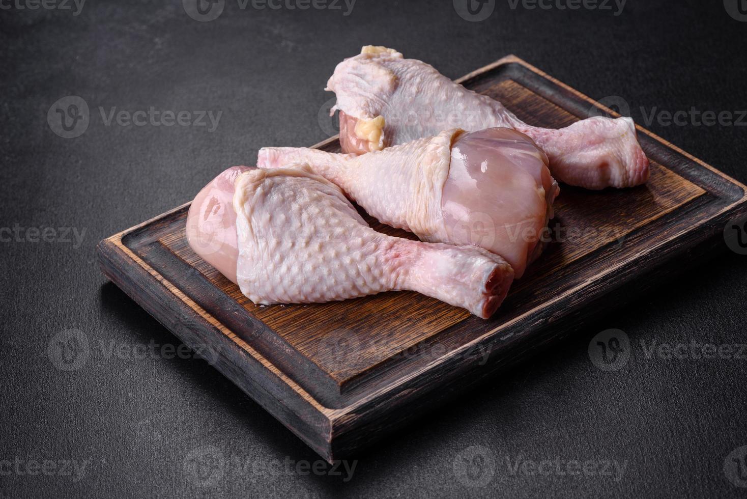 tres piernas de pollo crudo con especias y hierbas en una tabla de cortar de madera foto