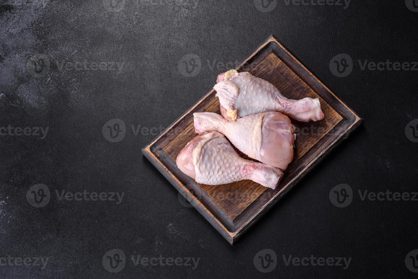 Three legs of raw chicken with spices and herbs on a wooden cutting board photo