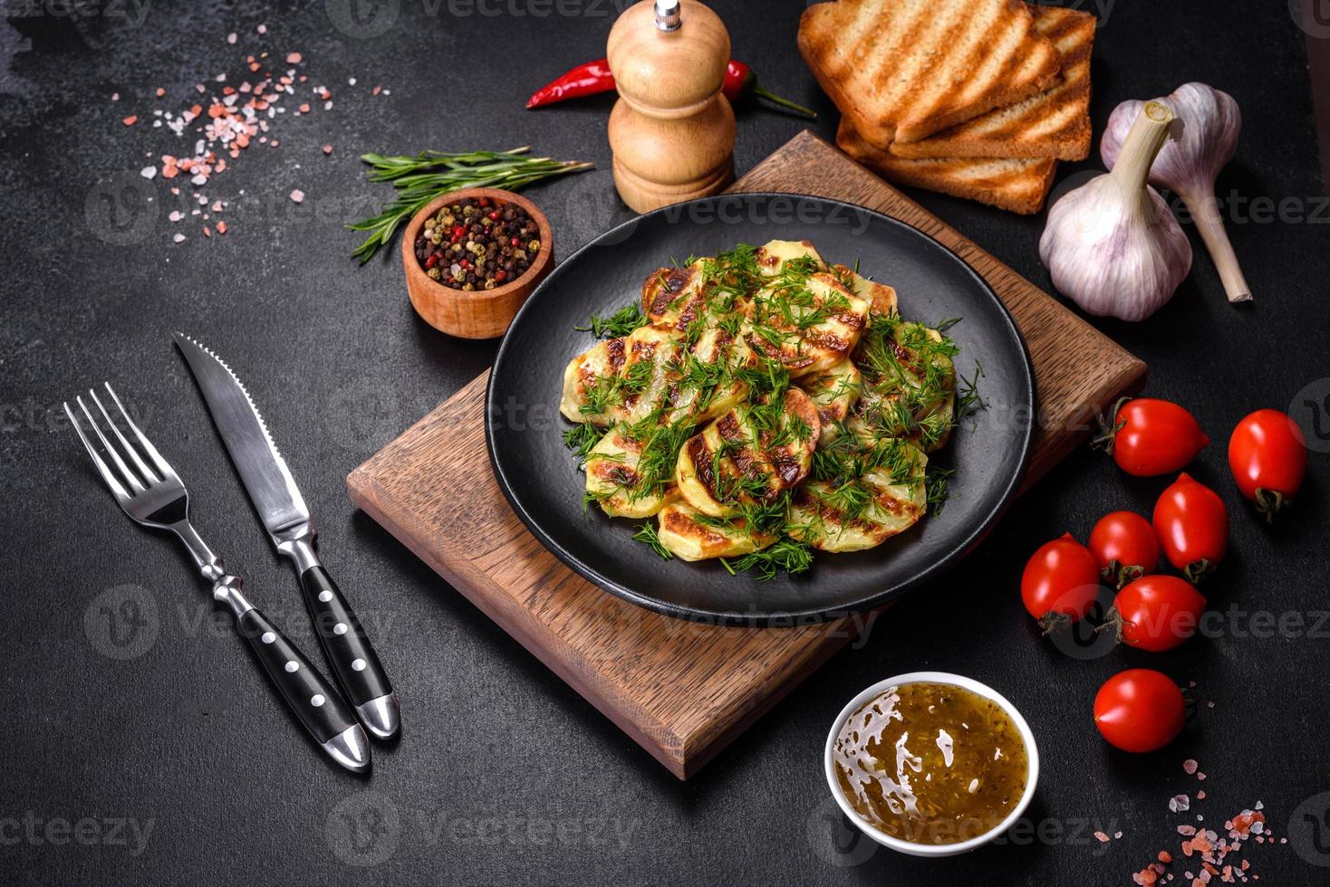 Delicious grilled potato slices with spices and herbs on a black plate photo