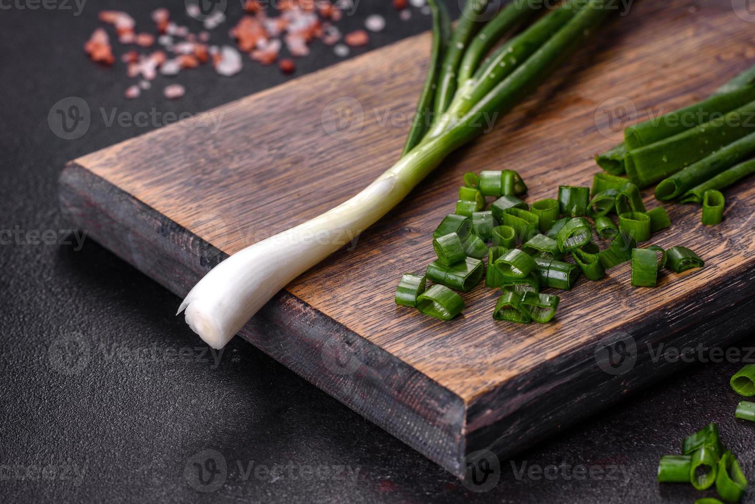 Fresh green onions on a cutting board. Dark concrete background photo