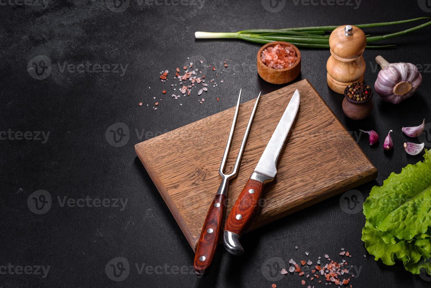 Fork, knife, spices and herbs, cutting board on a dark concrete background photo