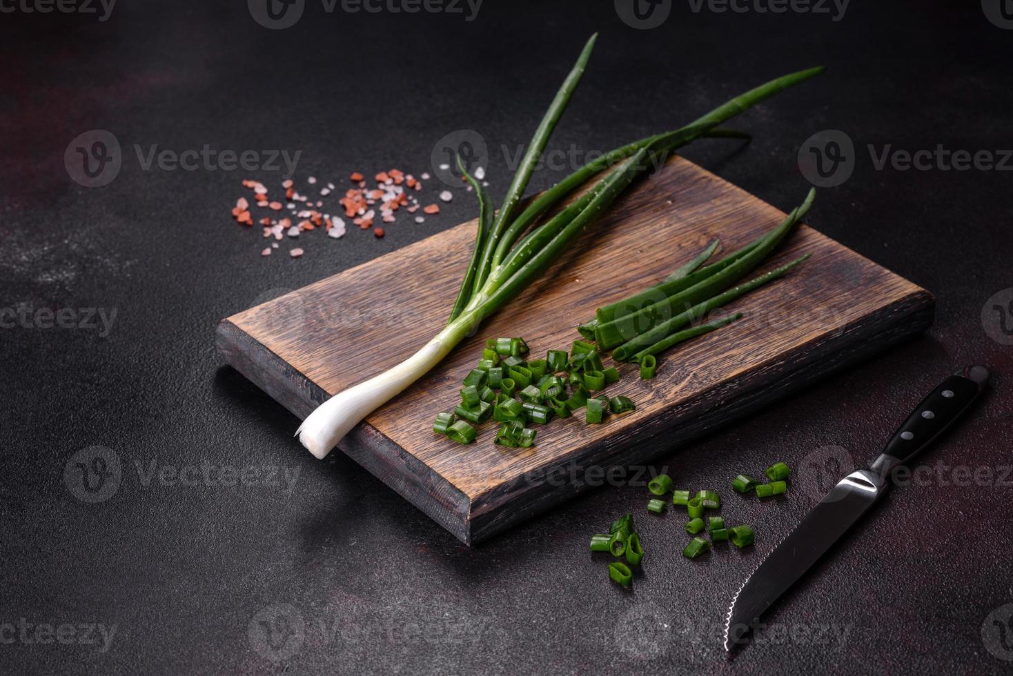 Fresh green onions on a cutting board. Dark concrete background photo