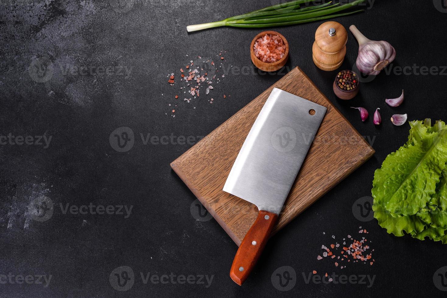 An axe for meat, spices and herbs, a cutting board against a dark concrete background photo