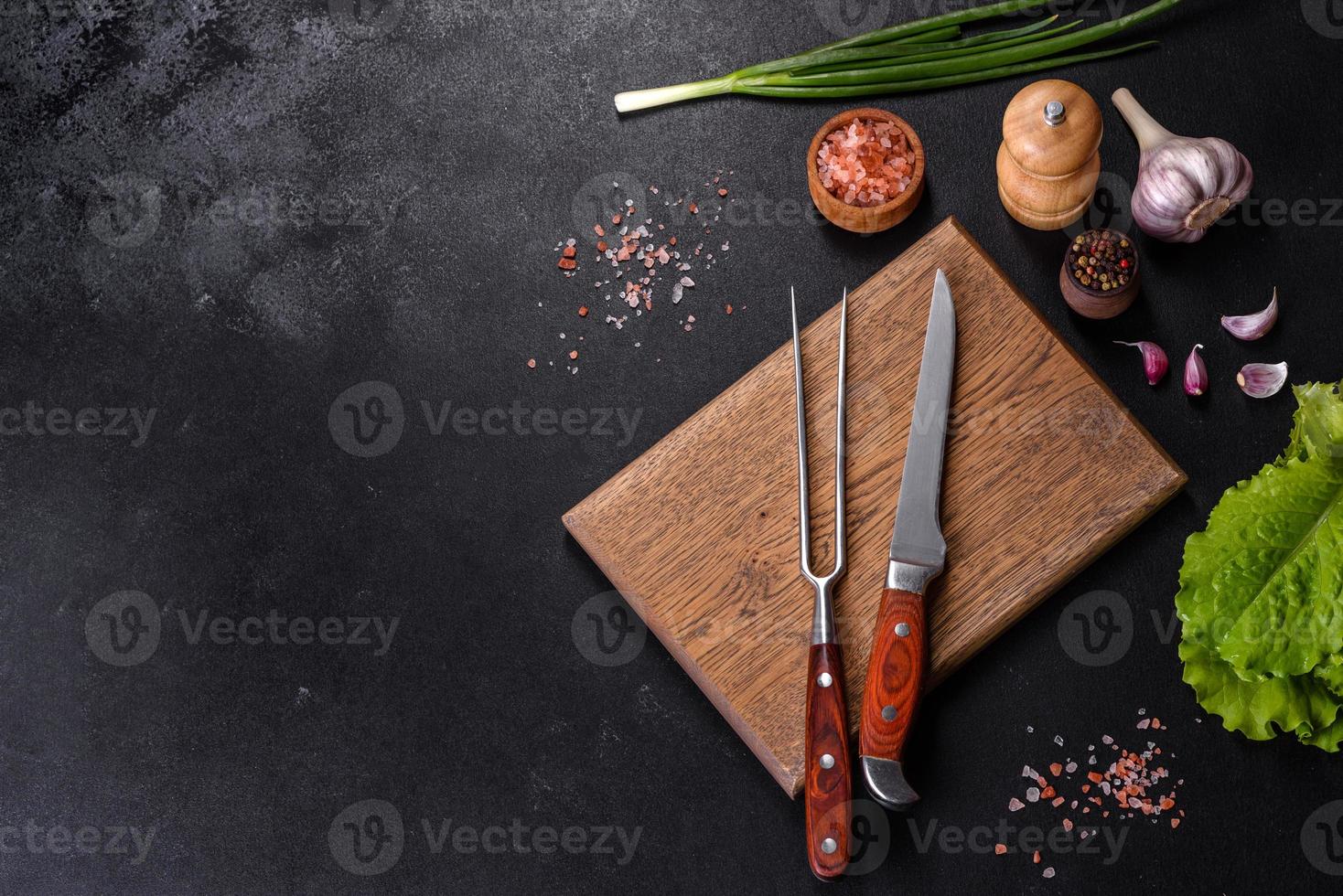 Fork, knife, spices and herbs, cutting board on a dark concrete background photo