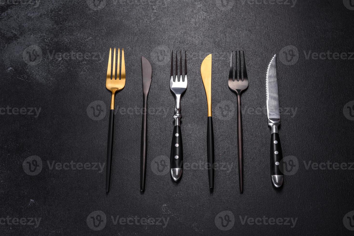 Several knives and forks in black gold and silver on a dark concrete background photo