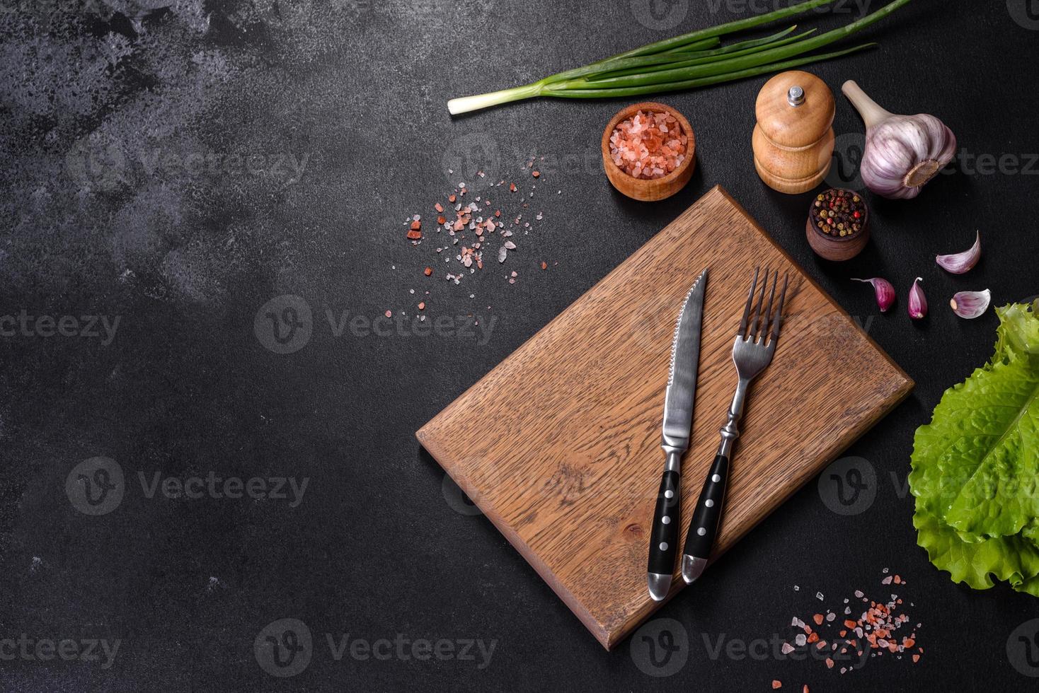 Fork, knife, spices and herbs, cutting board on a dark concrete background photo