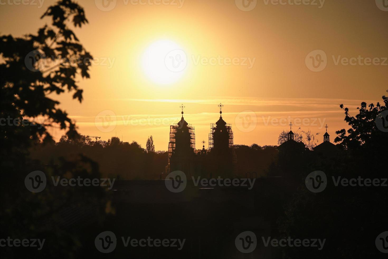 Kotryna's church with scaffolding for reconstruction silhouette in Vilnius orange and black sunset sky with tree branches and other buildings visible photo