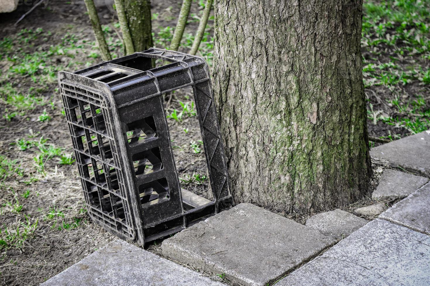 caja vieja de plástico negro para botellas destinadas al transporte de líquido parado cerca de un tronco de árbol en un día soleado al aire libre foto