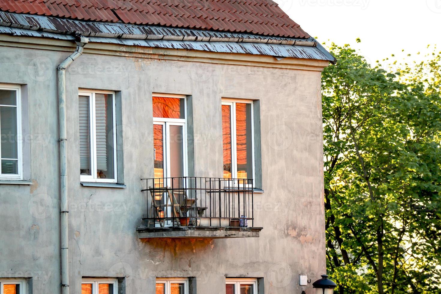 Old town building with sunset light reflecting in window and balcony door glass near green tree photo