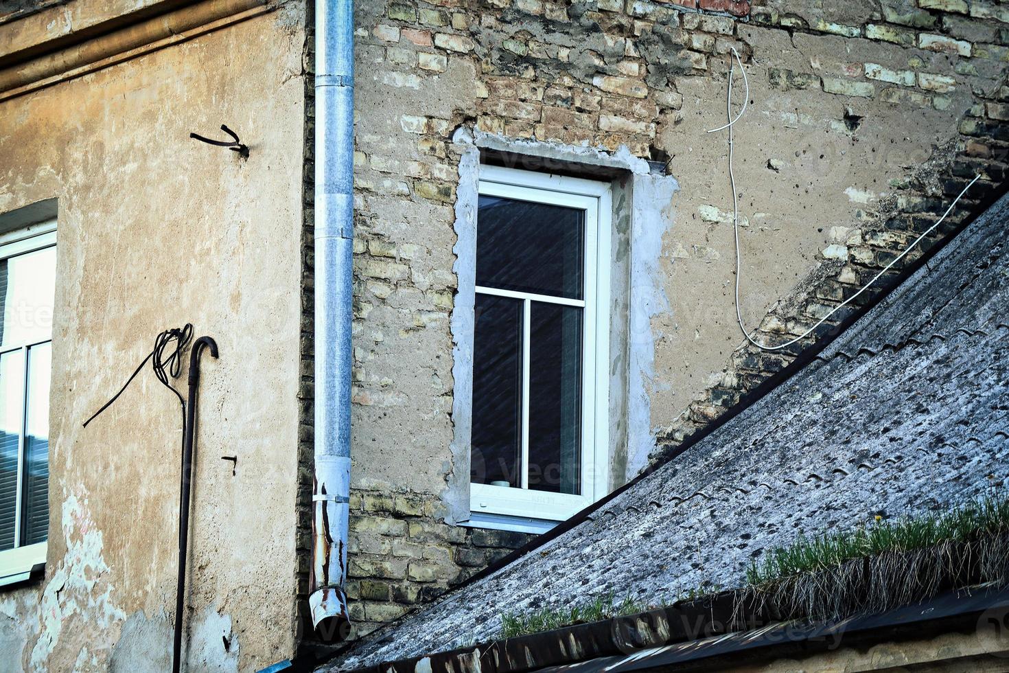 Window in an old brick house corner near the lower roof of another building. Weird architecture of an old town in Vilnius in Europe. photo