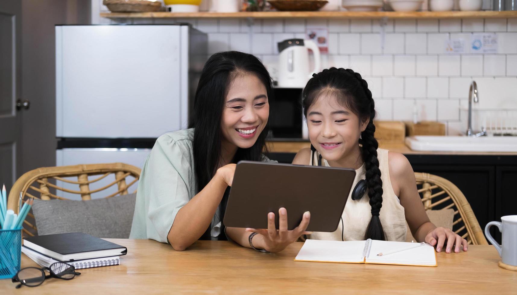 Mother and asian kid little girl learning and looking at laptop computer making homework studying with online education e-learning system.children video conference with teacher tutor at home photo