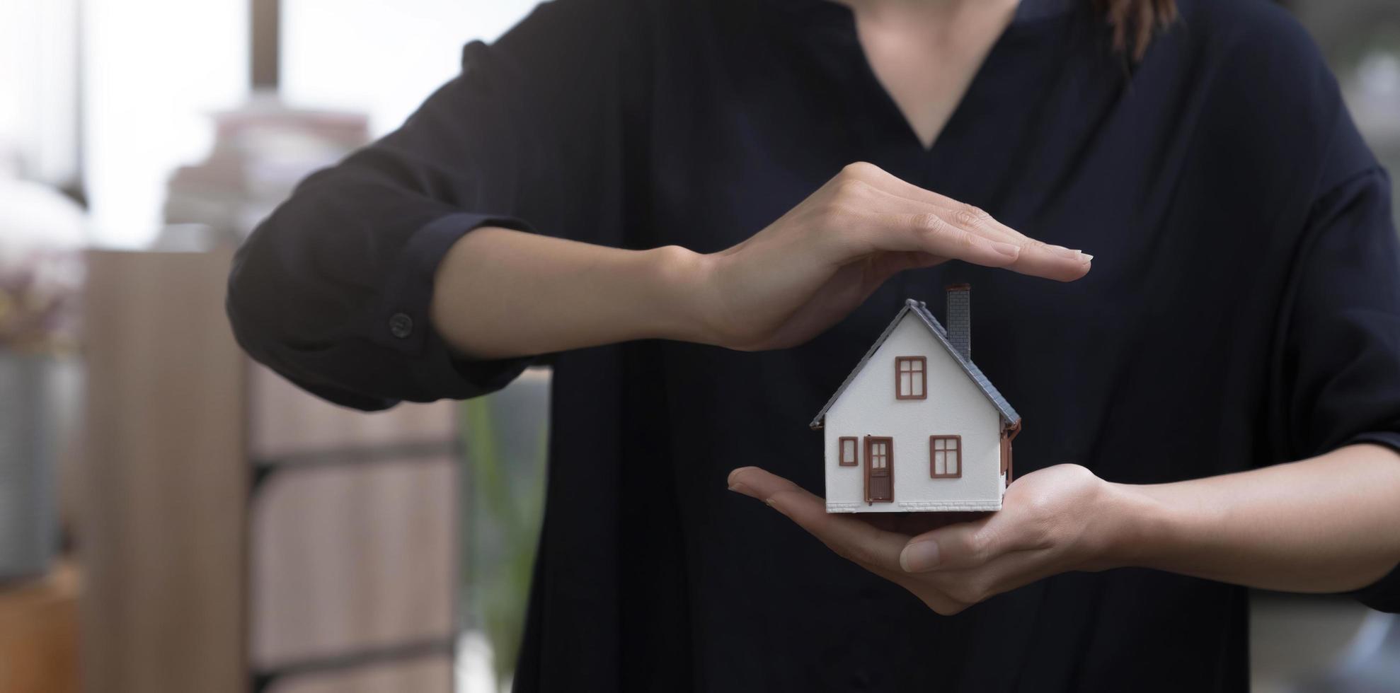 Property insurance and security concept. Protecting gesture of woman and symbol of the house. Wide banner composition with office in background. photo