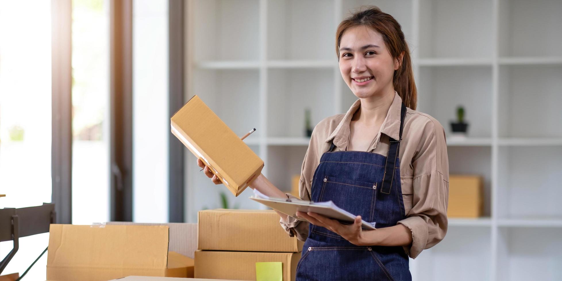 Young attractive asian woman owner startup business look at camera work happy with box at home prepare parcel delivery in sme supply chain photo