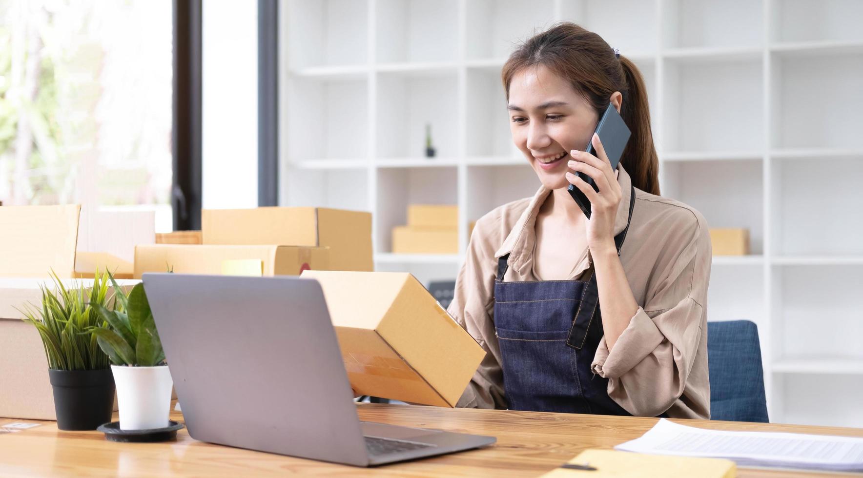 Startup small business entrepreneur or freelance Asian woman using a laptop with box, Young success Asian woman with her hand lift up, online marketing packaging box and delivery, SME concept. photo