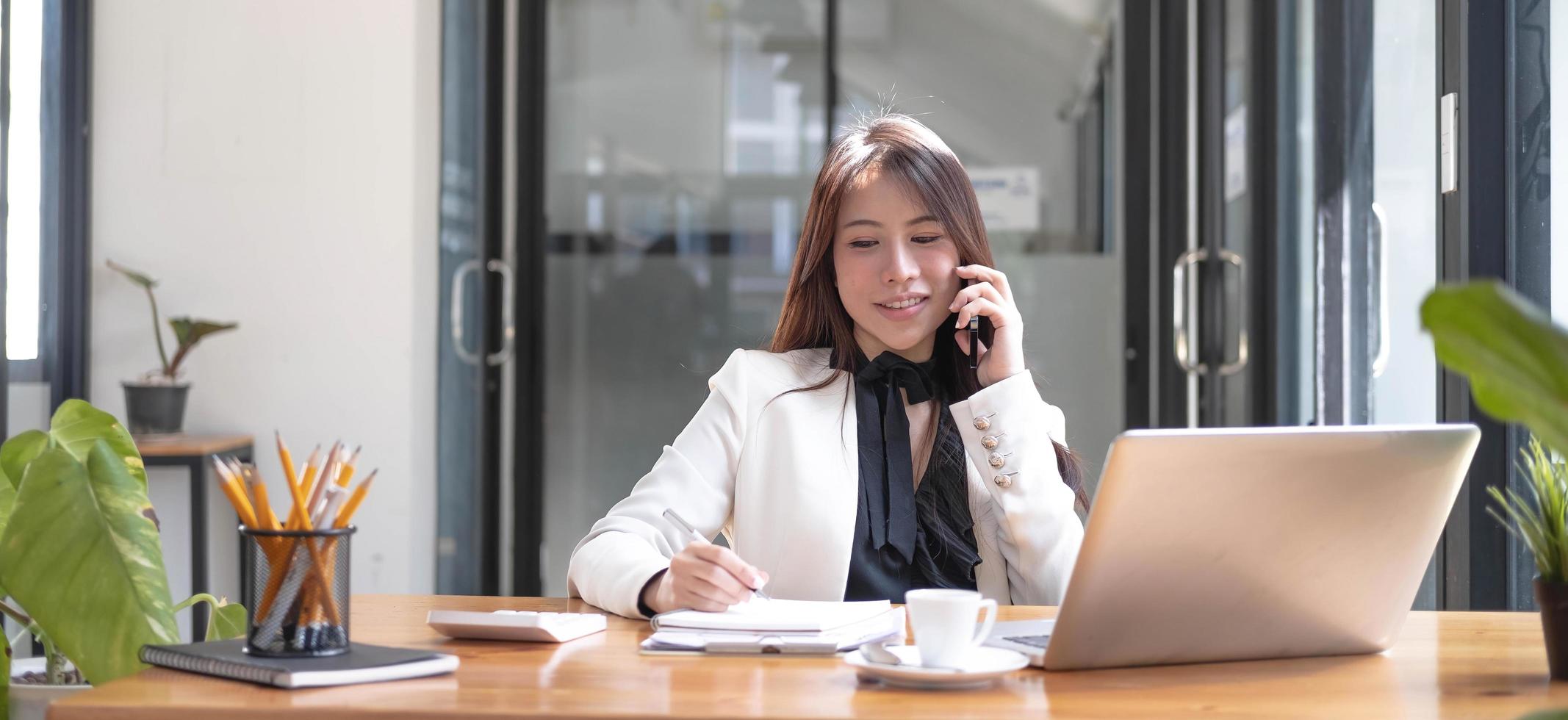 Beautiful young asian woman sitting at coffee shop using smartphone.  Happy young businesswoman sitting at table in cafe with tab top computer. photo