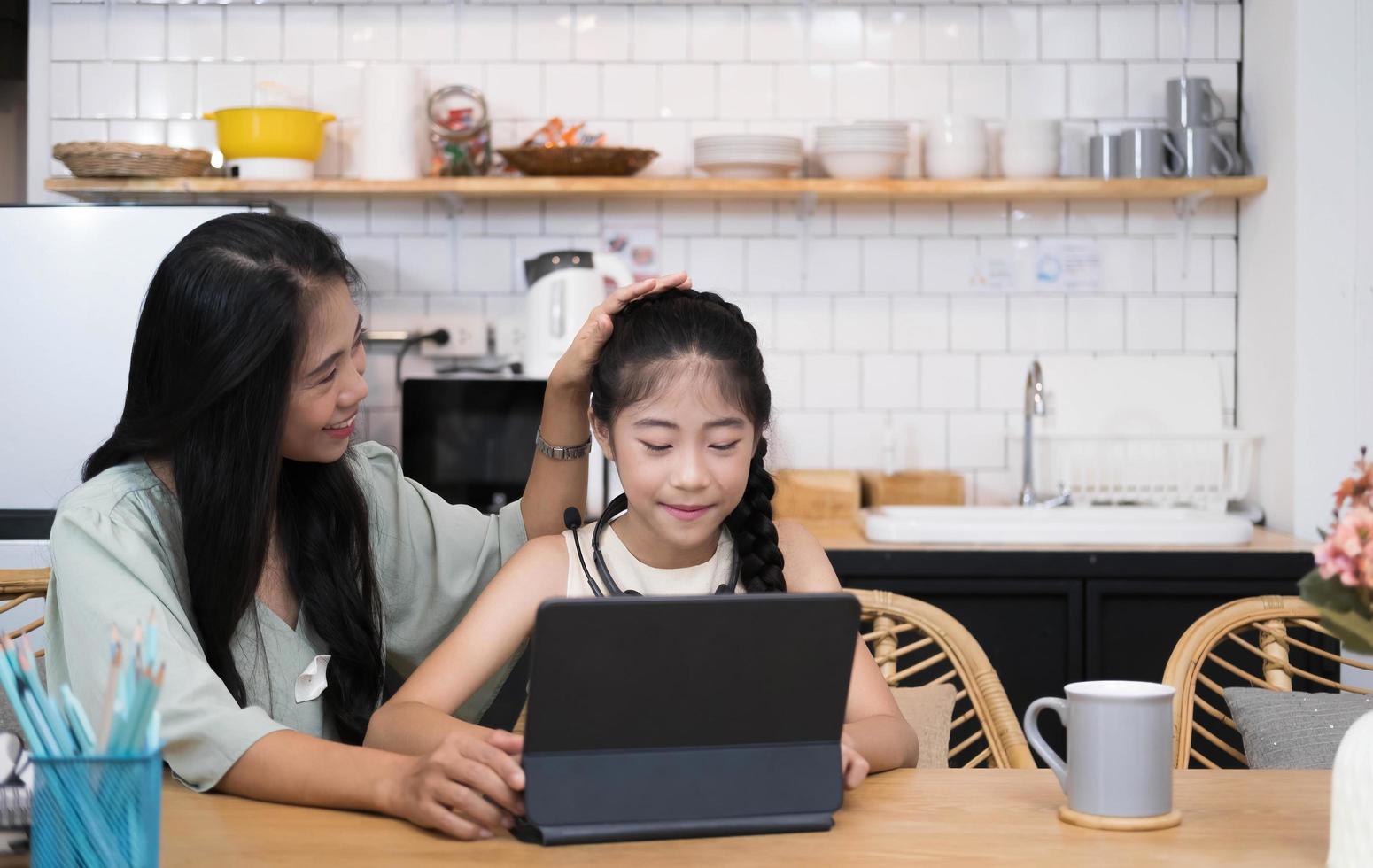 Mother and asian kid little girl learning and looking at laptop computer making homework studying with online education e-learning system.children video conference with teacher tutor at home photo