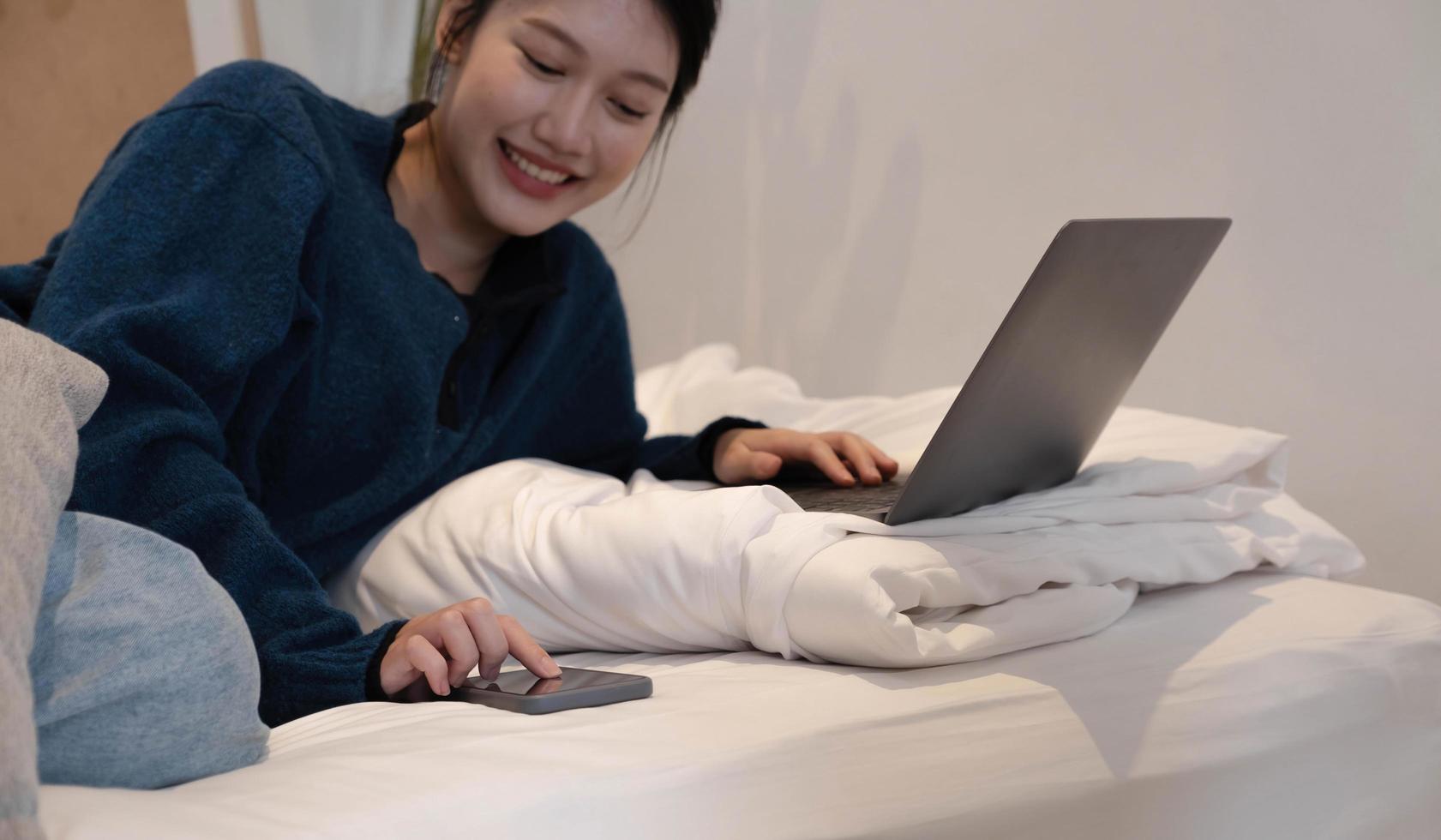 Portrait of an Asian woman lay down Playing Modern Technology phone in bed. Concept. Working at home. photo