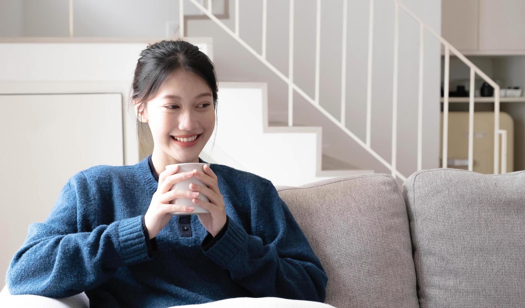 Portrait of smiling happy cheerful beautiful pretty asian woman relaxing drink. Girl felling enjoy having breakfast in holiday morning vacation on sofa at home photo