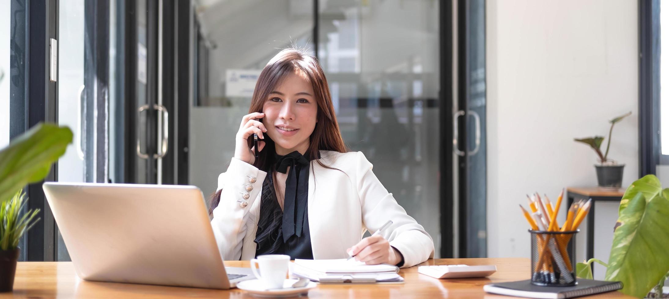 Charming Asian woman working at the office using smartphone and laptop Looking at the camera. photo