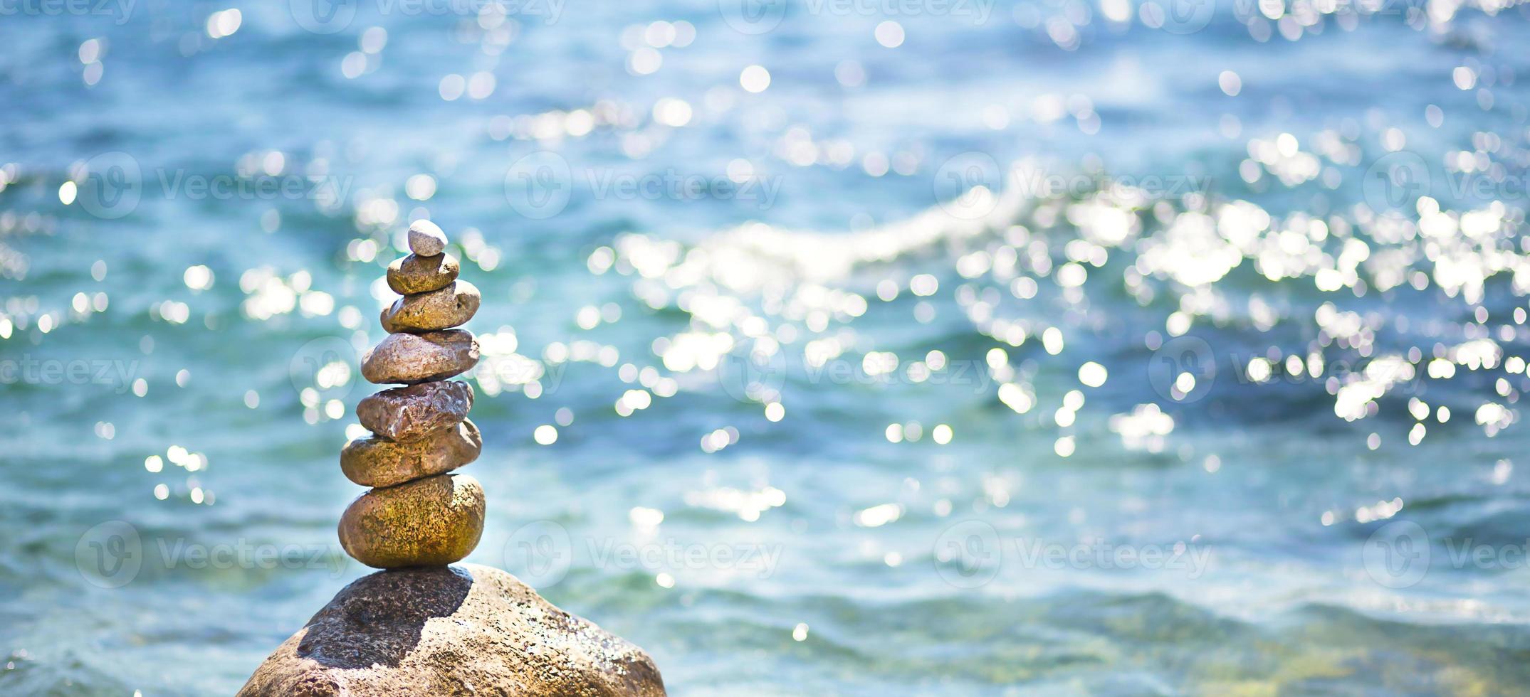 A pyramid of pebbles on a large stone against the background of the sea and the sun's glare on the water. Tour, tourism, vacation at the resort, swimming. Travel background, sunscreen. Copy space photo