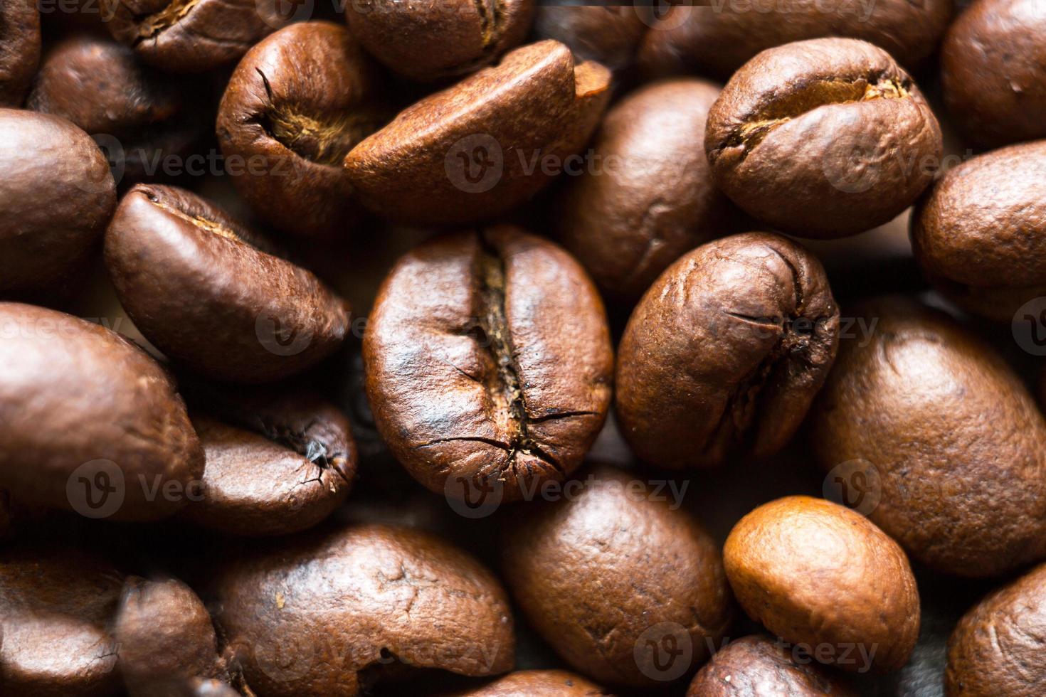 granos de café tostados cerca - fondo fragante. los granos de café arábica marrones están esparcidos sobre la mesa de madera. copie el espacio foto