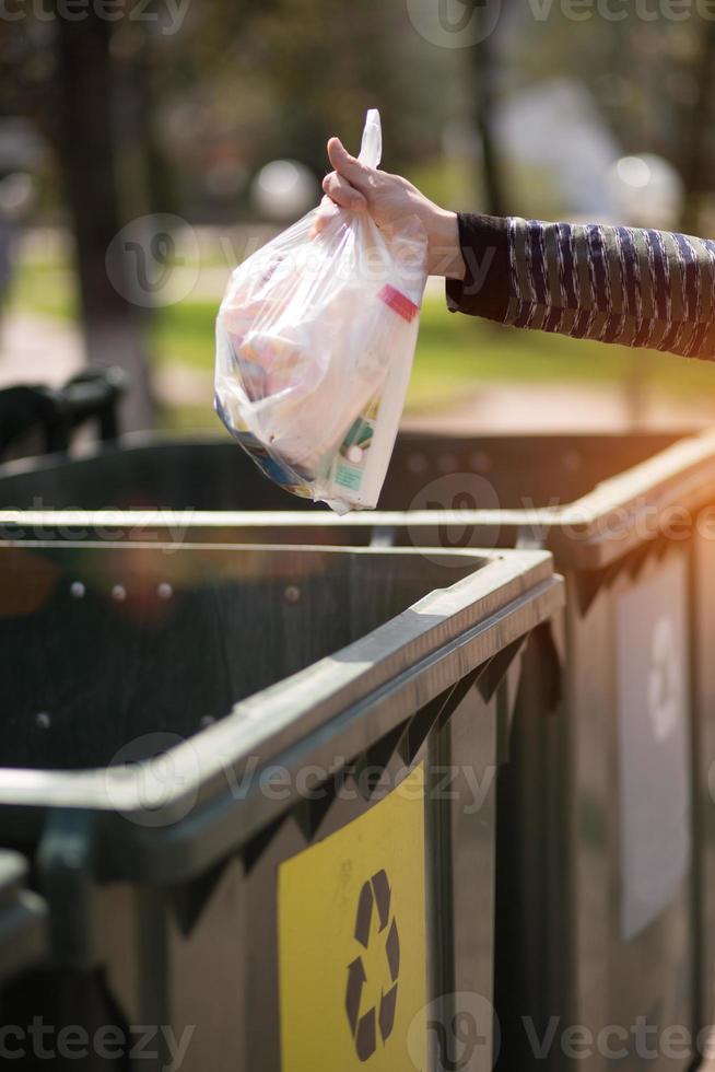 Hand with a bag of plastic garbage over containers for separation and sorting in Russia with the words Glass, plastic, household waste. photo