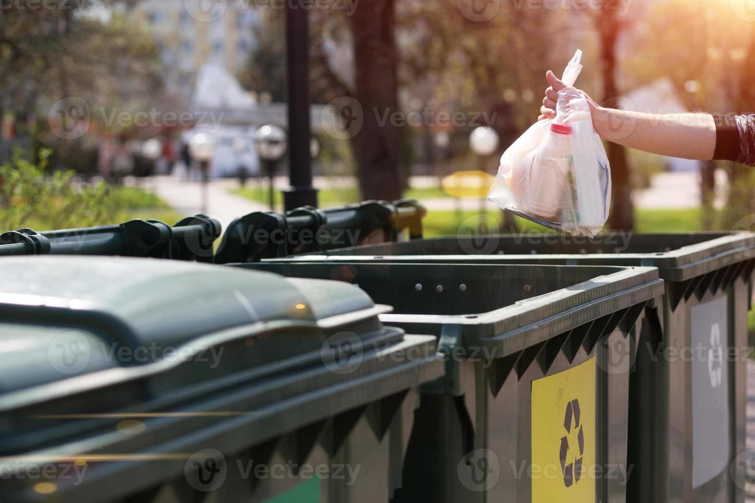 Hand with a bag of plastic garbage over containers for separation and sorting in Russia with the words Glass, plastic, household waste. photo