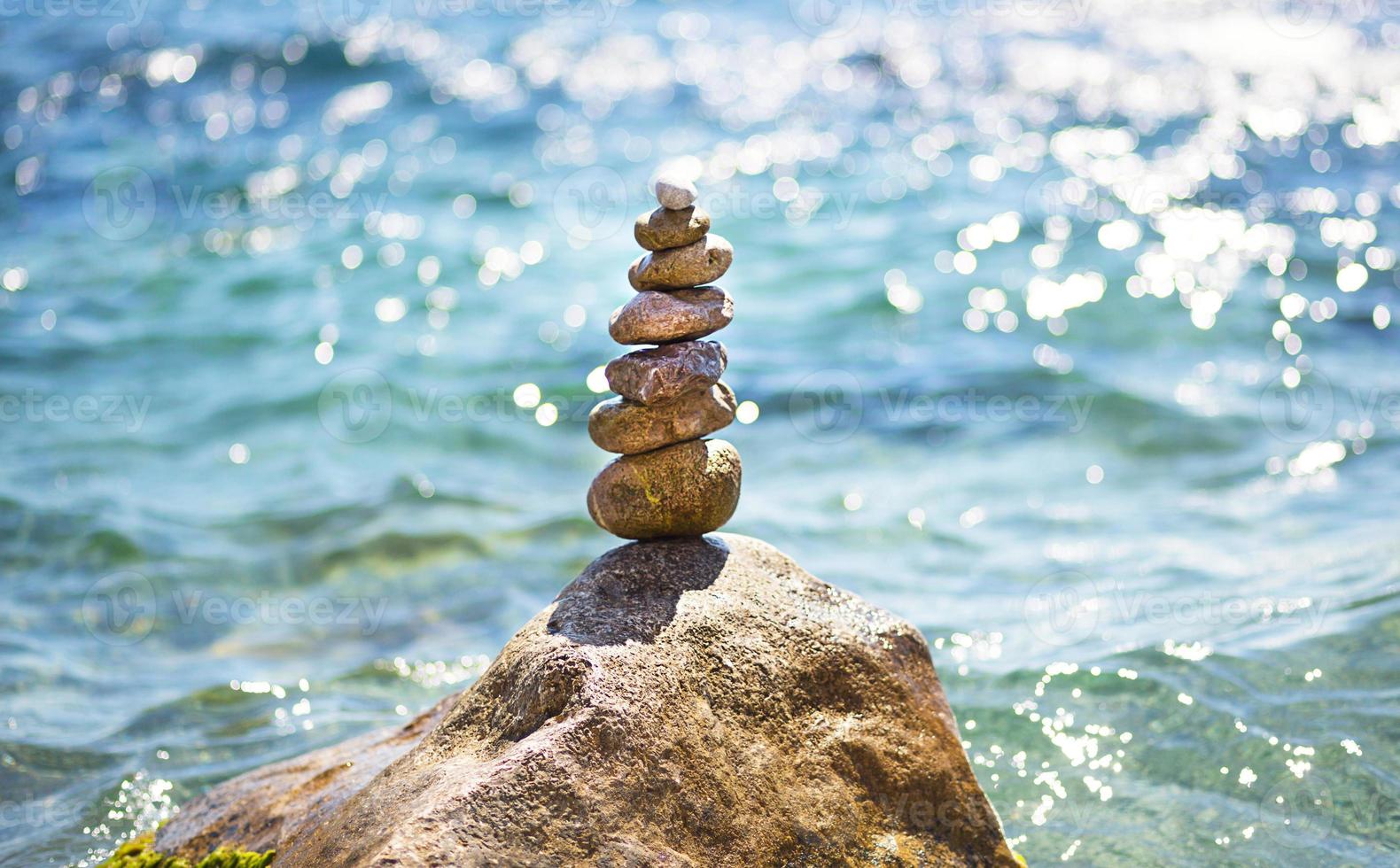 A pyramid of pebbles on a large stone against the background of the sea and the sun's glare on the water. Tour, tourism, vacation at the resort, swimming. Travel background, sunscreen. Copy space photo