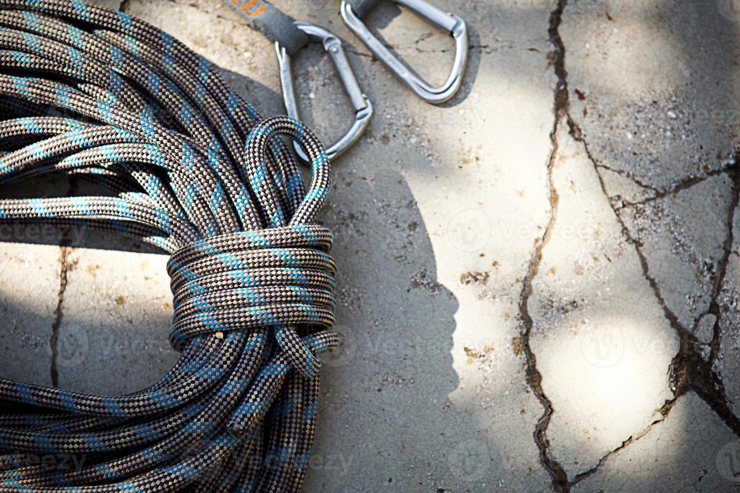 Coiled climbing rope and steel carabiner. Mountain climbing equipment harness, brakes, quickdraws, self-insurance, belay device eight. On a stone background with cracks. Flatlay, copy space photo