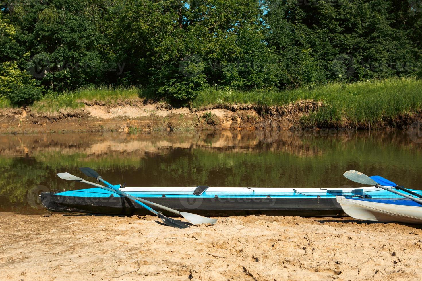 Tourist canoes with paddles stand on the river coast in summer on a water hike. Rafting on inflatable and frame double and triple kayak boats, family trip, extreme adventure in summer photo