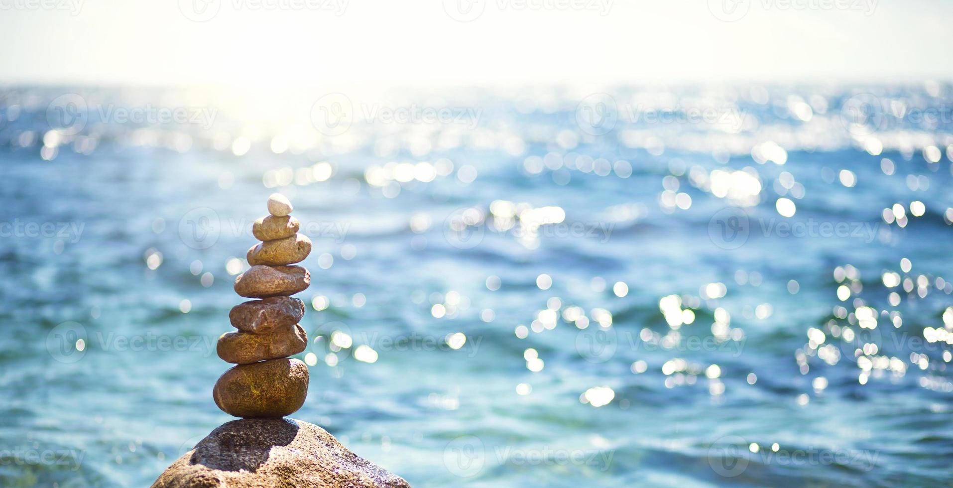 A pyramid of pebbles on a large stone against the background of the sea and the sun's glare on the water. Tour, tourism, vacation at the resort, swimming. Travel background, sunscreen. Copy space photo