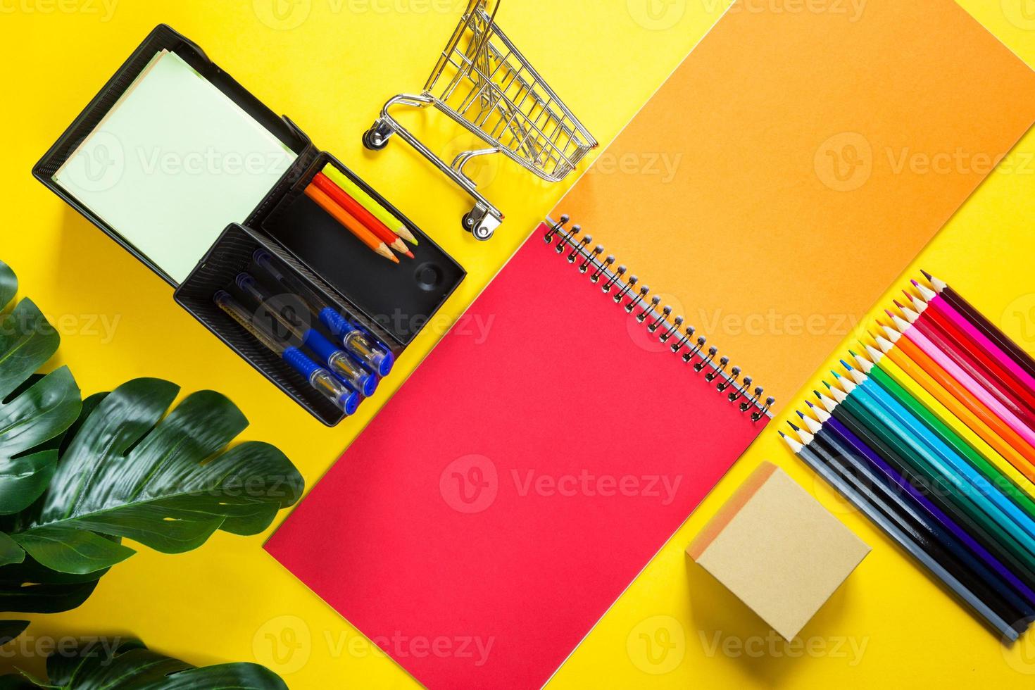 Layout of multi-colored stationery on a yellow background spiral notebook, colored pencils, stand, pens, indoor flower. Business flat lay, mock up. Sheets for notes, office work. Back to school photo