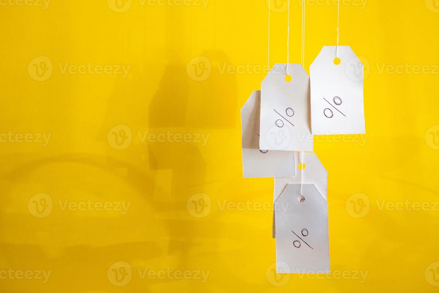 White tags with the percent sign hang on strings on a yellow background with shadows. Commerce, discount, sale, trade offer. Copy space, mock up. photo