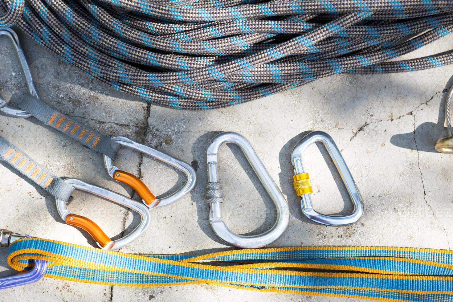 Coiled climbing rope and steel carabiner. Mountain climbing equipment harness, brakes, quickdraws, self-insurance, belay device eight. On a stone background with cracks. Flatlay, copy space photo