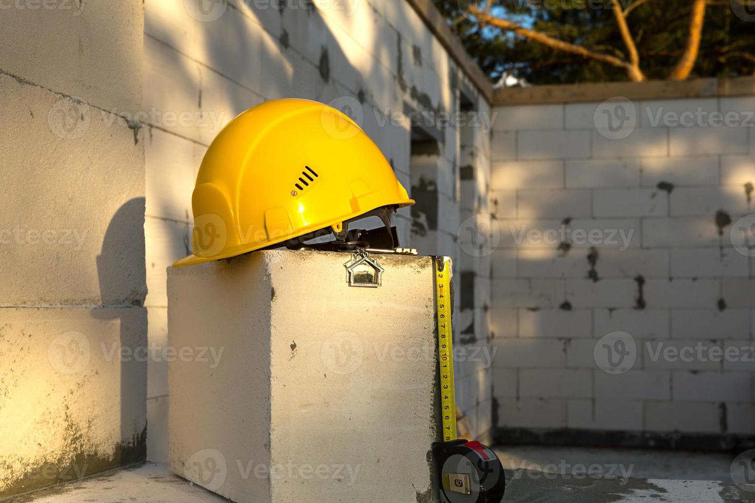 Construction yellow hardhat, key and a tape measure to house on window of housing made of blocks of porous concrete. Turnkey construction, future home, engineering, building. Work safety. Copy space photo