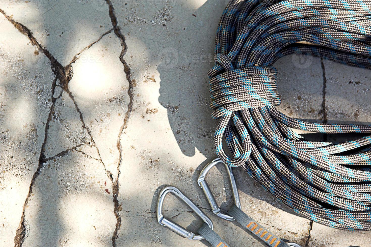 Coiled climbing rope and steel carabiner. Mountain climbing equipment harness, brakes, quickdraws, self-insurance, belay device eight. On a stone background with cracks. Flatlay, copy space photo