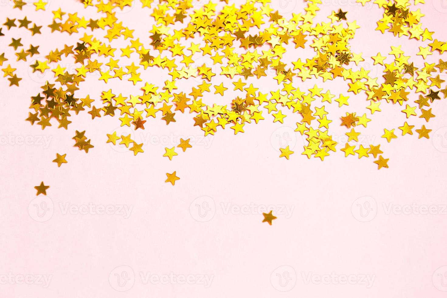 Gold sequins in the shape of stars shimmer on a pink background. Backgrounds with copyspace for a holiday, party decoration, Christmas and new year, birthday and anniversary. Gradient and texture photo