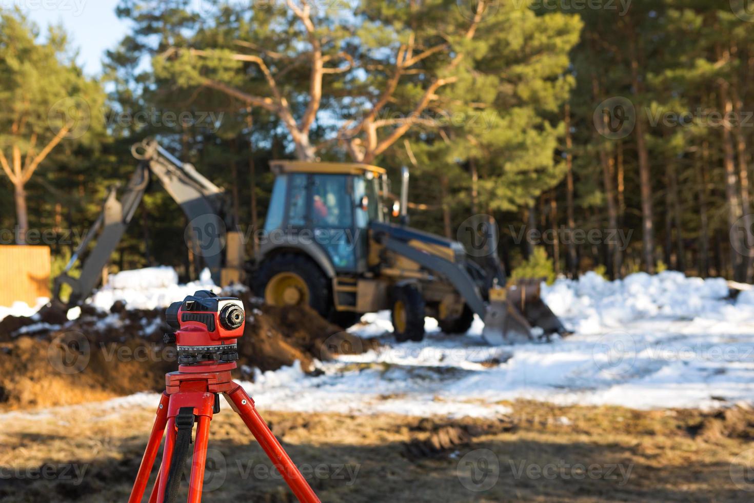 A geodesic level stands in front of a bulldozer for excavating a pit at a construction site. The excavator bucket digs a hole for building a house in the countryside. photo